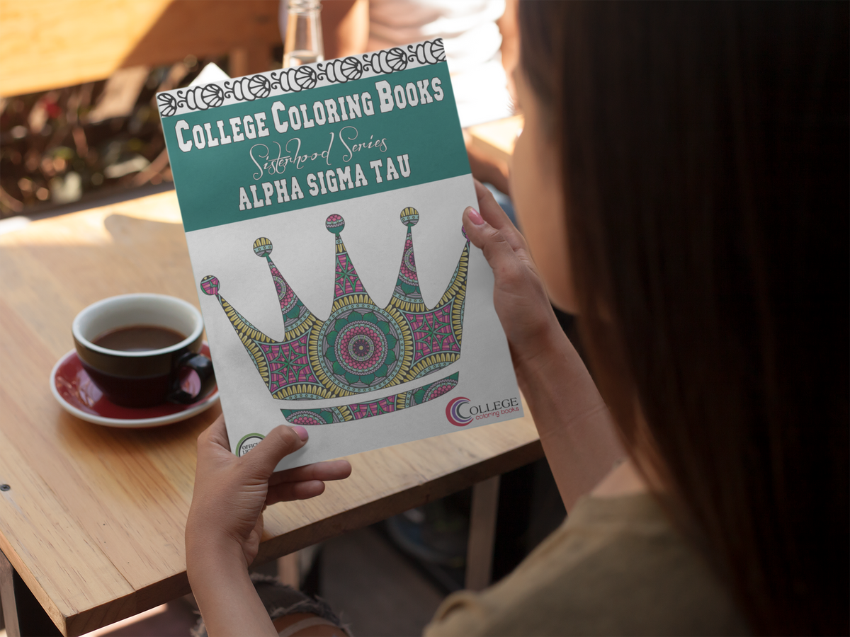 woman sitting at table with a cup of coffee holding an Alpha Sigma Tau coloring book